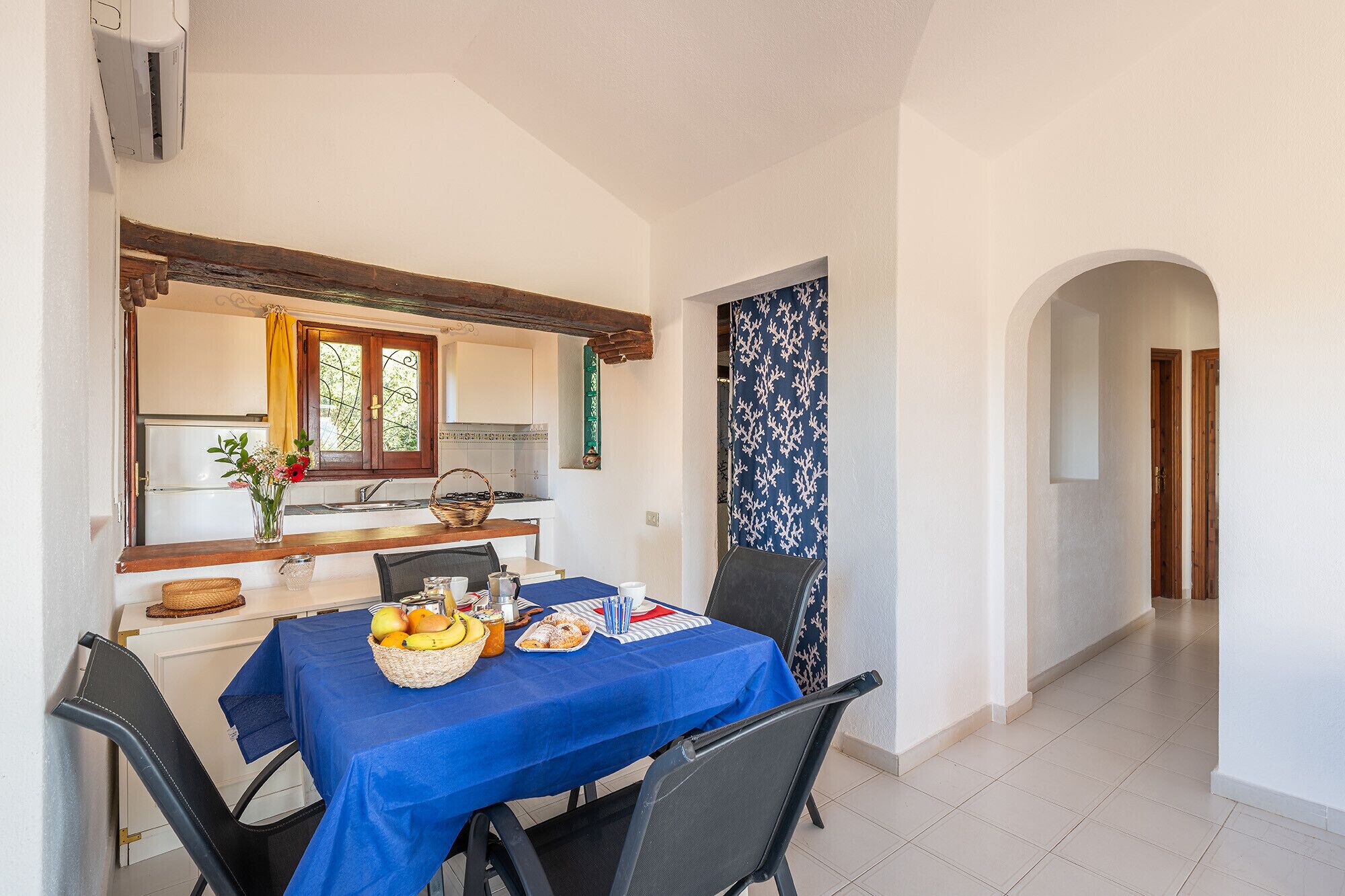 A dining area with a table set for two, a kitchen in the background, and a hallway leading to another room.