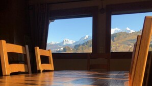 A room with wooden flooring and large windows offering a view of snow-capped mountains. - Huge Chalet in Combloux, sleeps up to 14, 5mins access to huge Evasion ski area. (Combloux)