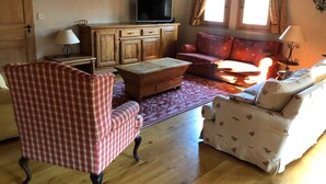 A cozy living room with wooden furniture, a television, and a red patterned sofa. - Huge Chalet in Combloux, sleeps up to 14, 5mins access to huge Evasion ski area. (Combloux)