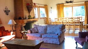 A cozy living room with a wooden ceiling, a sofa set, a dining table with chairs, and a fireplace. - Huge Chalet in Combloux, sleeps up to 14, 5mins access to huge Evasion ski area. (Combloux)