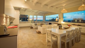A spacious kitchen with a dining area, large windows, and a view of the sunset.