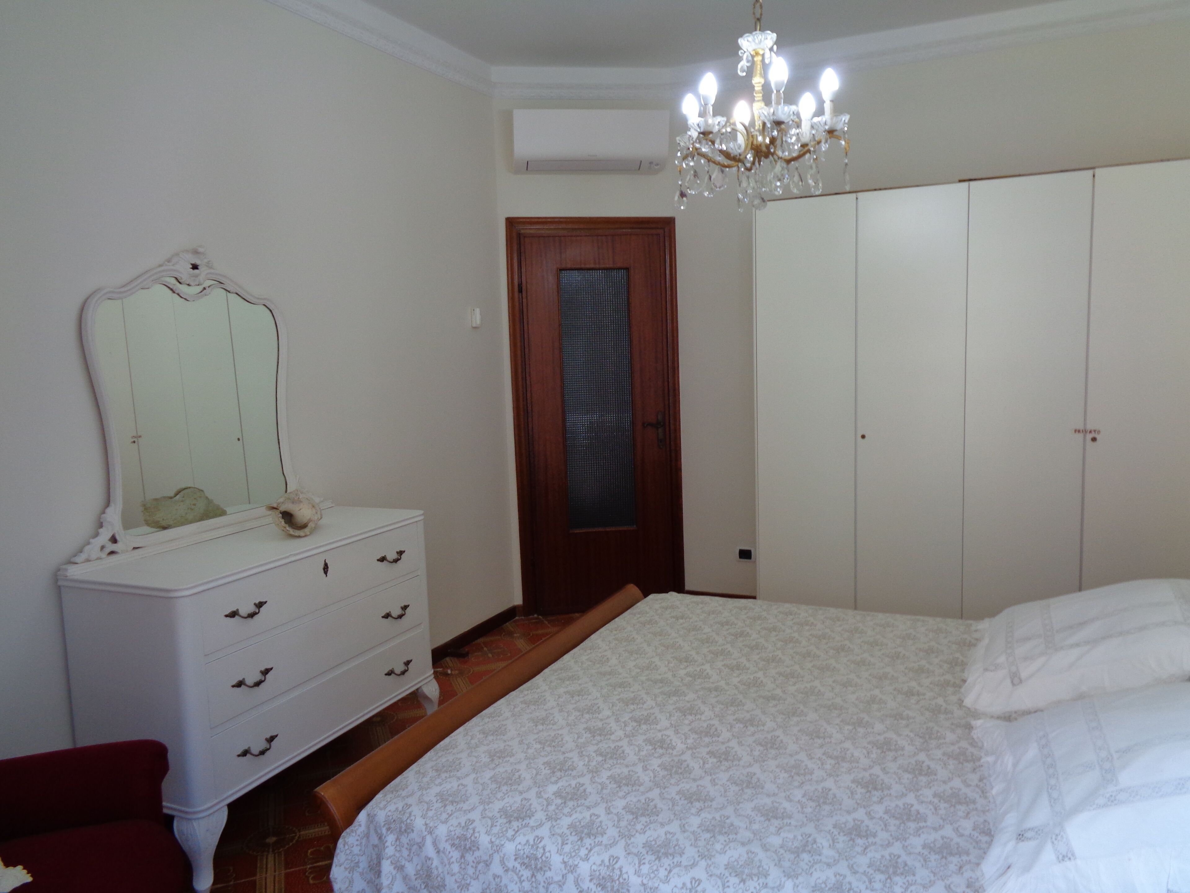 Une chambre à coucher comprenant un lit, une commode, un miroir, une armoire et un lustre.