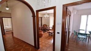 Un passadís amb un paviment motllurat, una zona de dinar amb taula i cadires, i un dormitori amb llit i cortines.