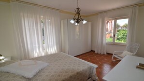 Un dormitori amb un llit, una cadira, una taula i una finestra amb cortines.
