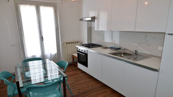 A compact kitchen with a gas stove, oven, and sink. There is a glass table with chairs and a door leading to a balcony. - The house of Ambra, 100m. from beach, balconies-parking-wi-fi- A. C.- ascens (LEVANTO)