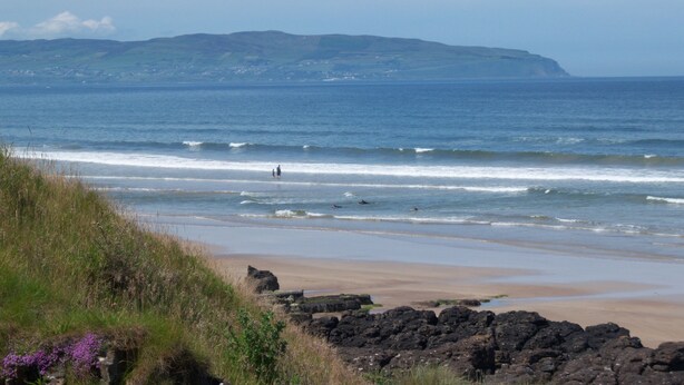 A coastal beach with rocky foreground, waves, and distant hills. - Sea front Apartment In Castlerock, With Stunning Panoramic Views (Castlerock)