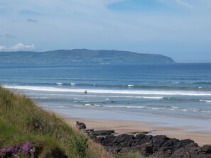 A coastal beach with rocky foreground, waves, and distant hills. - Sea front Apartment In Castlerock, With Stunning Panoramic Views (Castlerock)