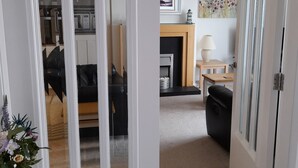 A modern living room with a fireplace, a dining area, and a kitchen visible through an open door. - Sea front Apartment In Castlerock, With Stunning Panoramic Views (Castlerock)