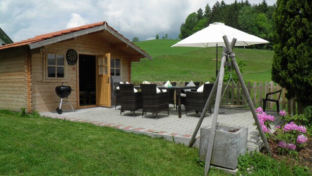 Una cabaña de madera con un patio, una parrilla y mobiliario exterior.