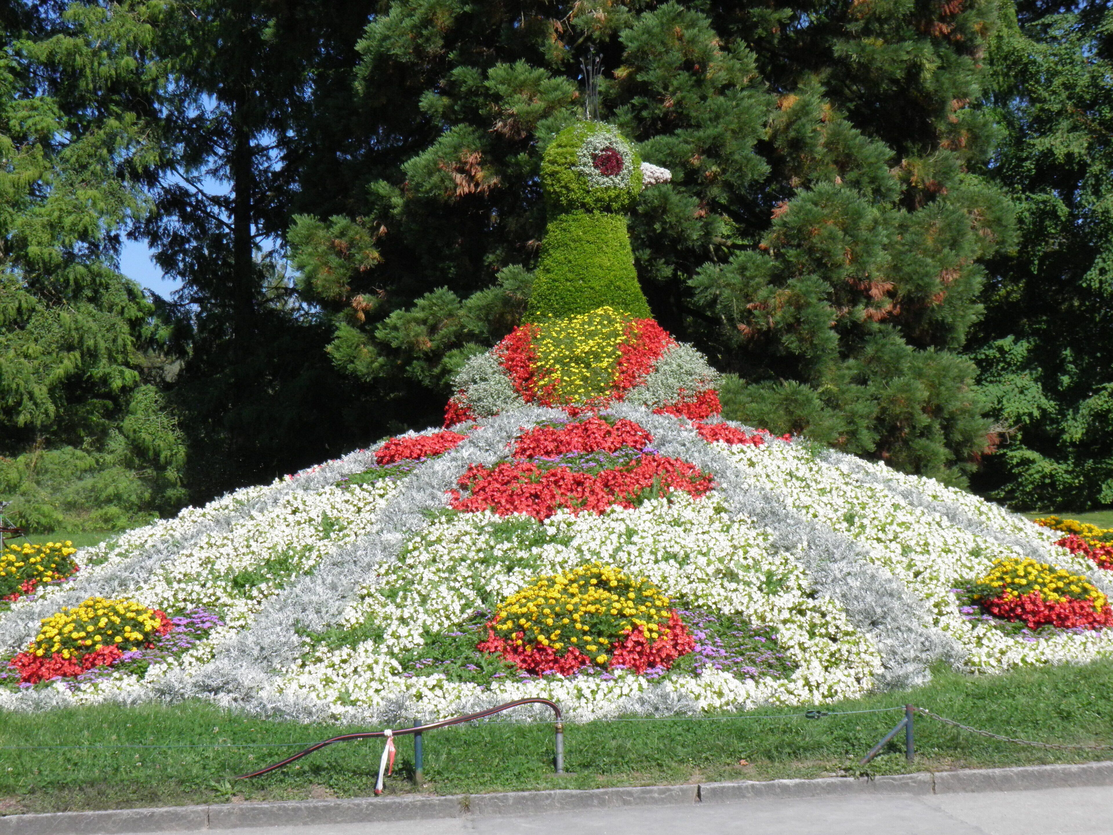 Un arreglo floral piramidal de gran tamaño con diversos colores, rodeado de árboles.