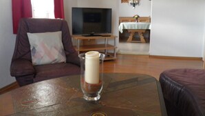 Una sala de estar con un sofá de cuero marrón, una mesa de vidrio con una vela, un televisor y una zona de comedor con una mesa y sillas de madera.