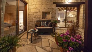A cozy outdoor seating area with stone flooring, a cushioned sofa, a small round table, and potted plants.