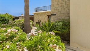 A stone building with a balcony, surrounded by lush greenery and flowering plants.