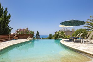 A swimming pool with lounge chairs and an umbrella, surrounded by greenery and a view of the sea. - 'Owls Watch Villa' -  A Stone Built Villa that sleeps 6 guests  in 3 bedrooms (Paphos)