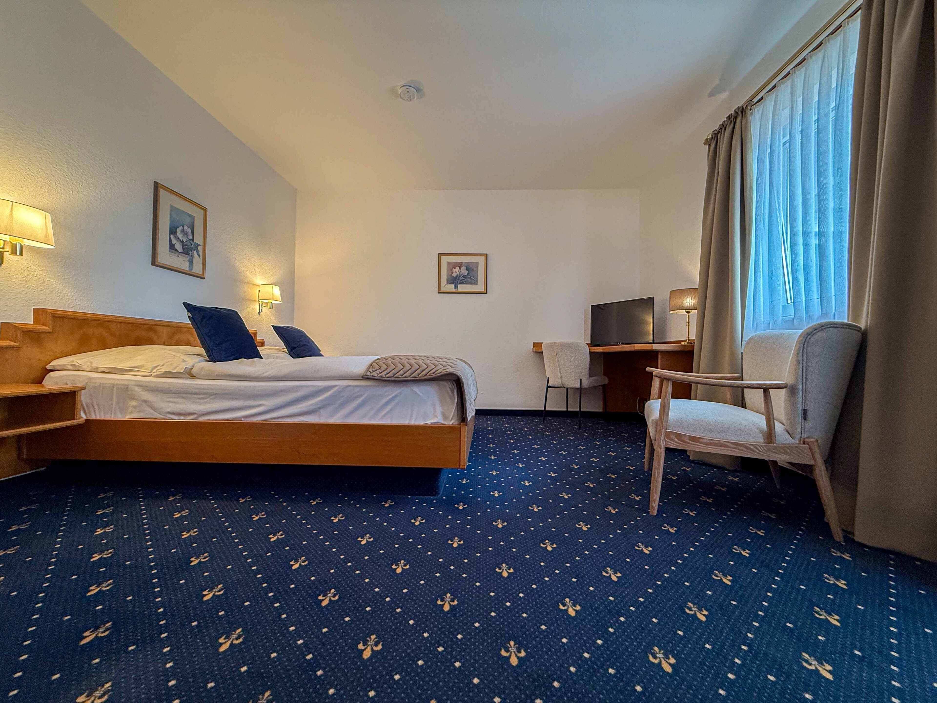 A hotel room with a bed, a desk, a chair, and a TV.