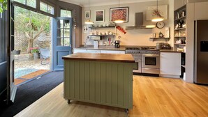 Una cocina moderna con una isla grande, electrodomésticos integrados y vista al jardín a través de la puerta abierta.