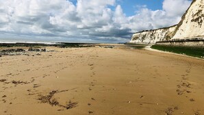 Una playa arenosa con huellas y un acantilado al fondo.