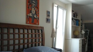 Ein Schlafzimmer mit einem Holz-Kopfteil, zwei Betten mit blau karierten Kissen, einem Fenster mit Vorhang und einem Bücherregal mit Büchern und einem Globus.