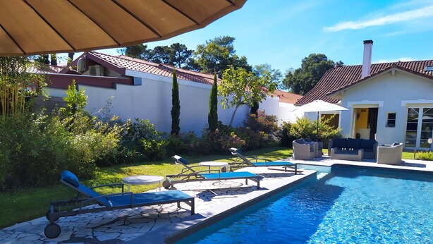 Ein Pool mit Liegestühlen, eine Steinterrasse und ein Gartenbereich mit Bäumen und Sträuchern.