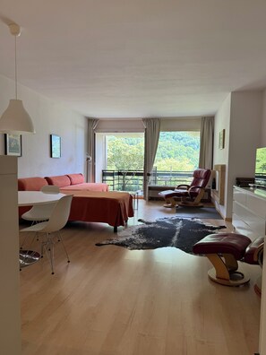 A spacious room with a bed, a dining table, a chair, a sofa, a massage chair, and a view of the outdoors.
