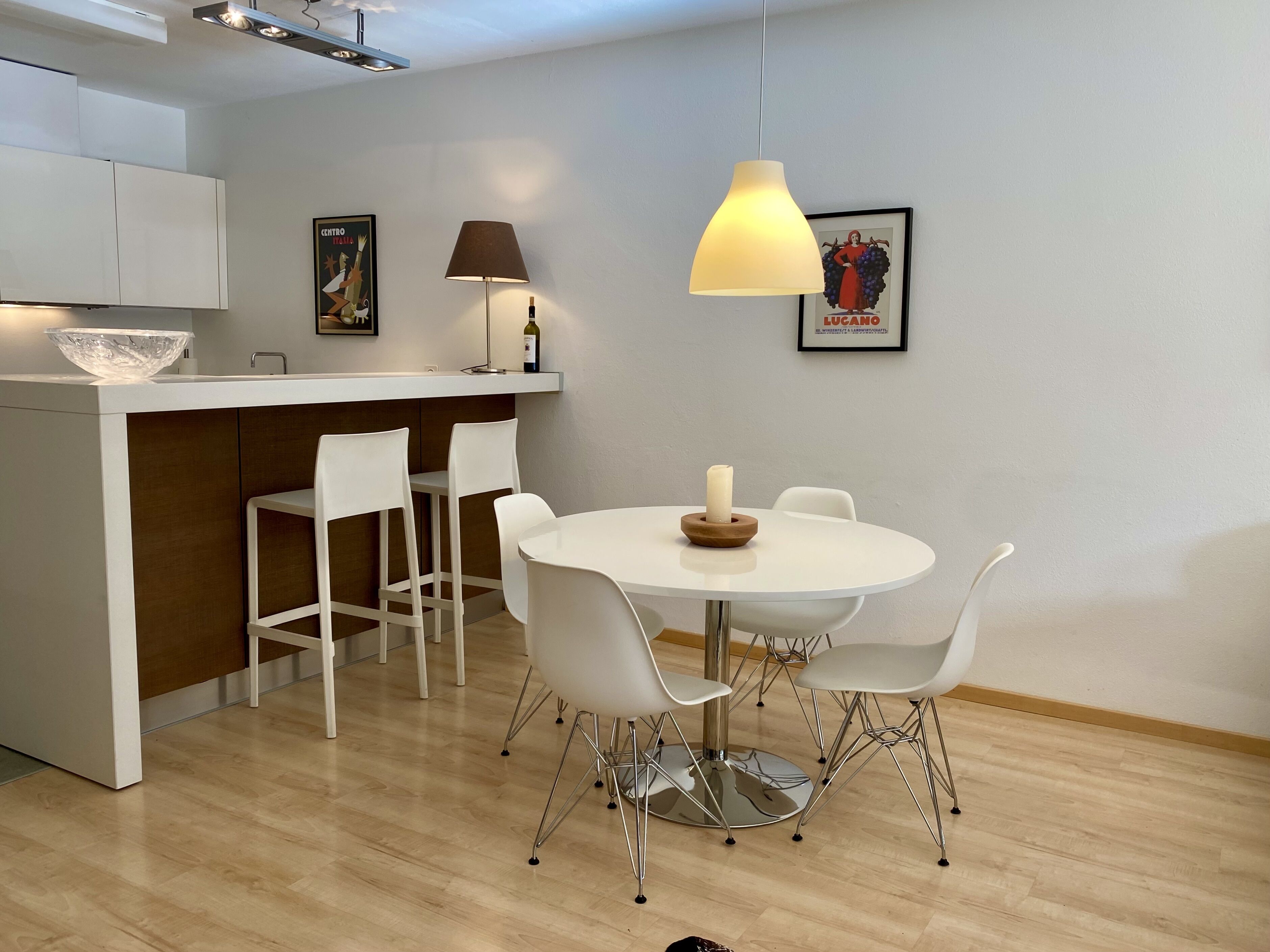A modern kitchen with white cabinets, a central island, and a dining area with a round table and white chairs.