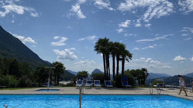 A swimming pool with lounge chairs, palm trees, and mountains in the background.