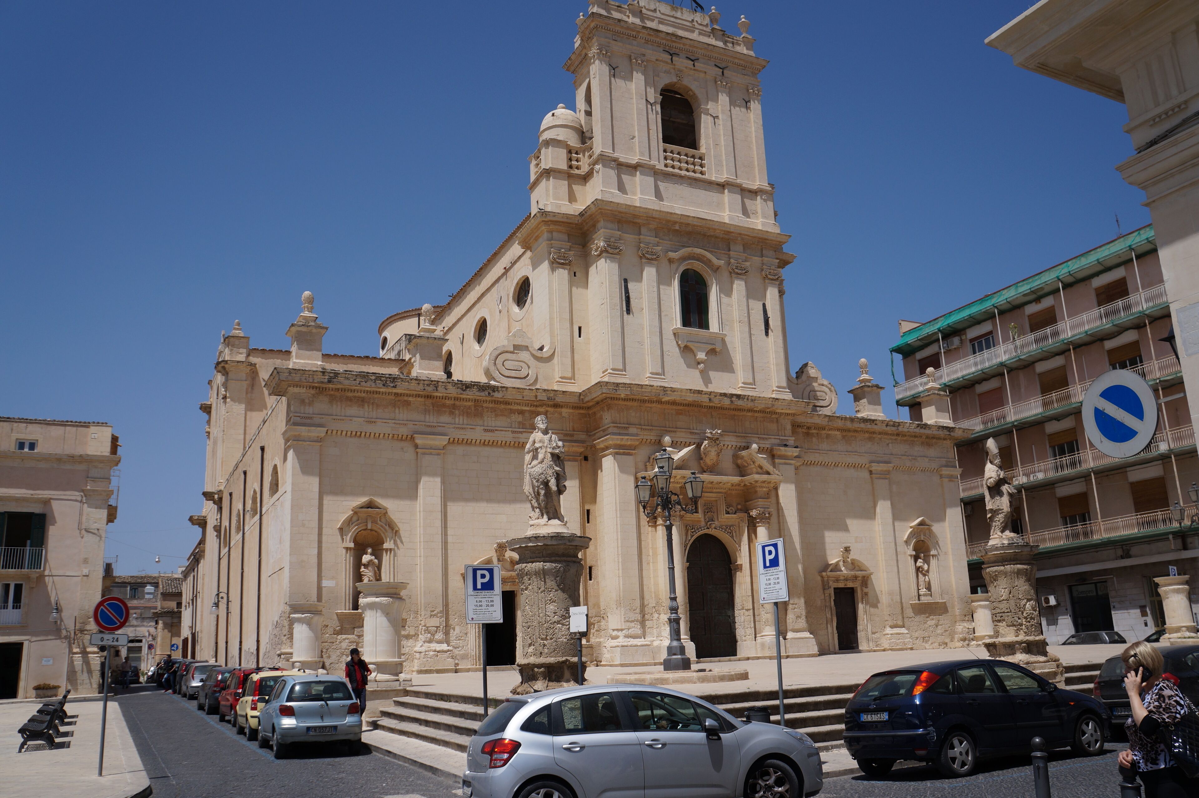 A historic building with a prominent bell tower, a statue in front, and a parking sign.