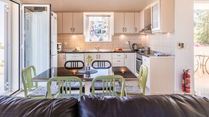 Uma cozinha moderna com área de refeições, com uma mesa de vidro, cadeiras verdes e vista pela janela.