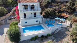 Um edifício de dois andares com piscina, área de estar externa e um muro de contenção de pedra.