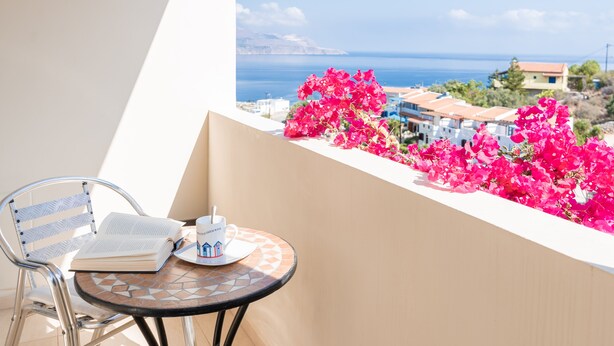 Varanda com vista para o mar, uma mesa, uma cadeira e um livro.