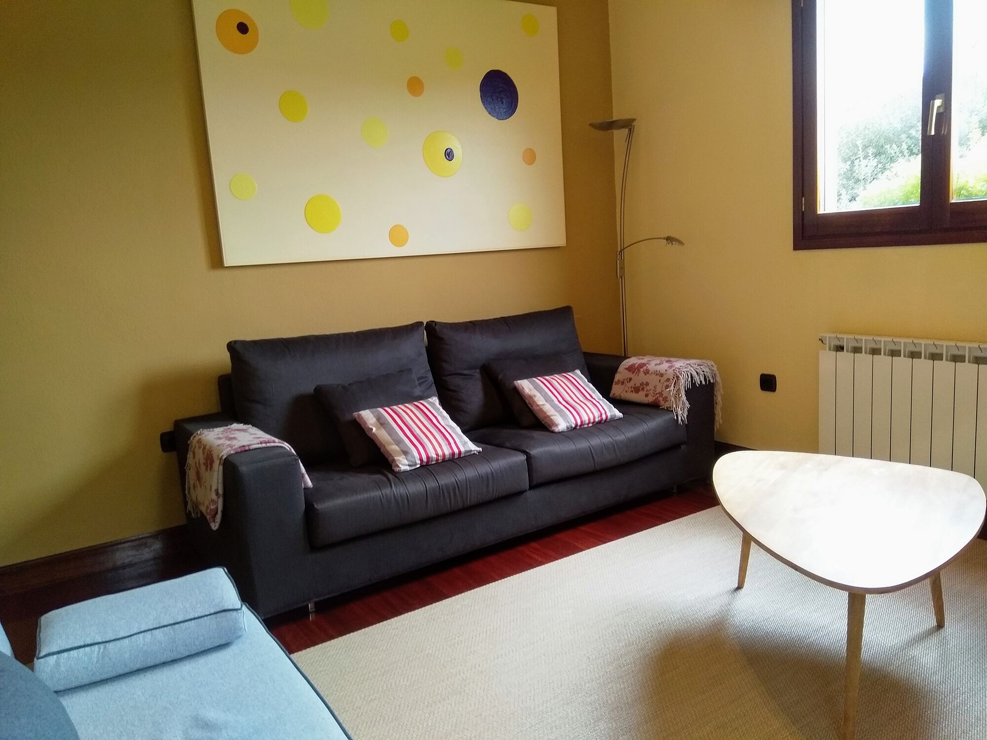 A living room with a black sofa, a white coffee table, and a large abstract painting on the wall.