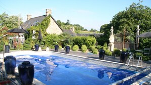 A swimming pool with a wooden deck, surrounded by stone buildings and greenery. - Luxurious Gite in tranquil surroundings with private heated salt water pool (Louvigne-Du-Desert)