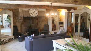 A living room with a stone wall, a large clock, a fireplace, a sofa, and a television. - Luxurious Gite in tranquil surroundings with private heated salt water pool (Louvigne-Du-Desert)