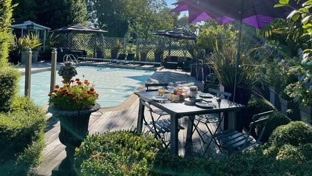 A wooden deck with a pool, surrounded by lush greenery and a pergola with umbrellas. - Luxurious Gite in tranquil surroundings with private heated salt water pool (Louvigne-Du-Desert)