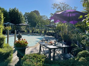 A wooden deck with a pool, surrounded by lush greenery and a pergola with umbrellas. - Luxurious Gite in tranquil surroundings with private heated salt water pool (Louvigne-Du-Desert)