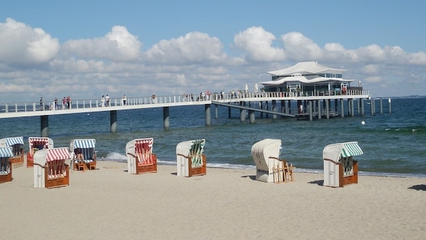 Une jetée avec des chaises de plage et un bâtiment doté d’un toit blanc.