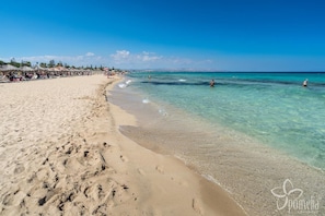 A beach with clear turquoise water, sandy shore, and umbrellas.