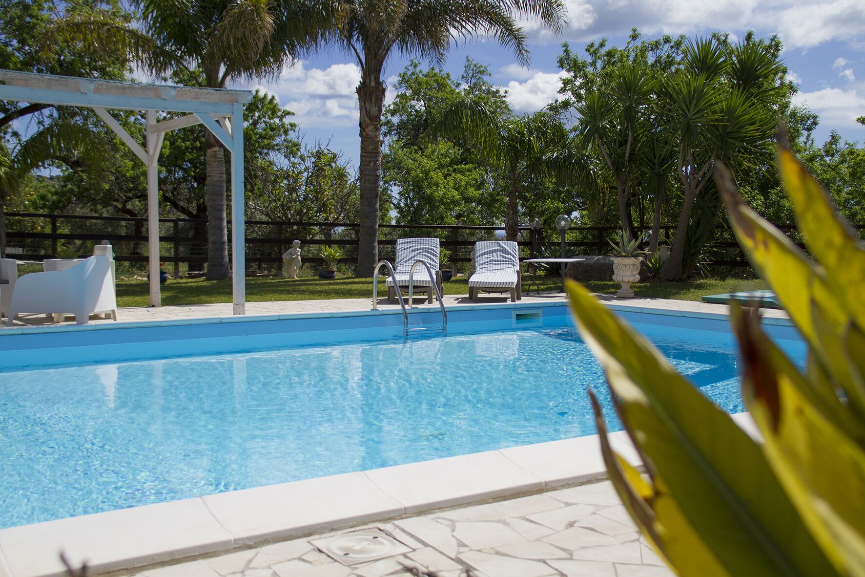 Una piscina con sillas de descanso y una pérgola.
