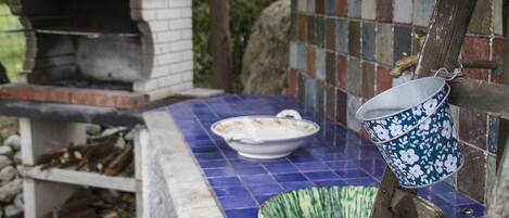 A rustic outdoor kitchen with a brick oven, a blue tiled table, and a hanging flower pot.