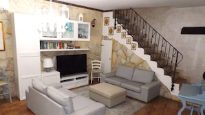 A living room with a TV, sofas, a staircase, and a stone wall. - House / Villa - Avola (Avola)