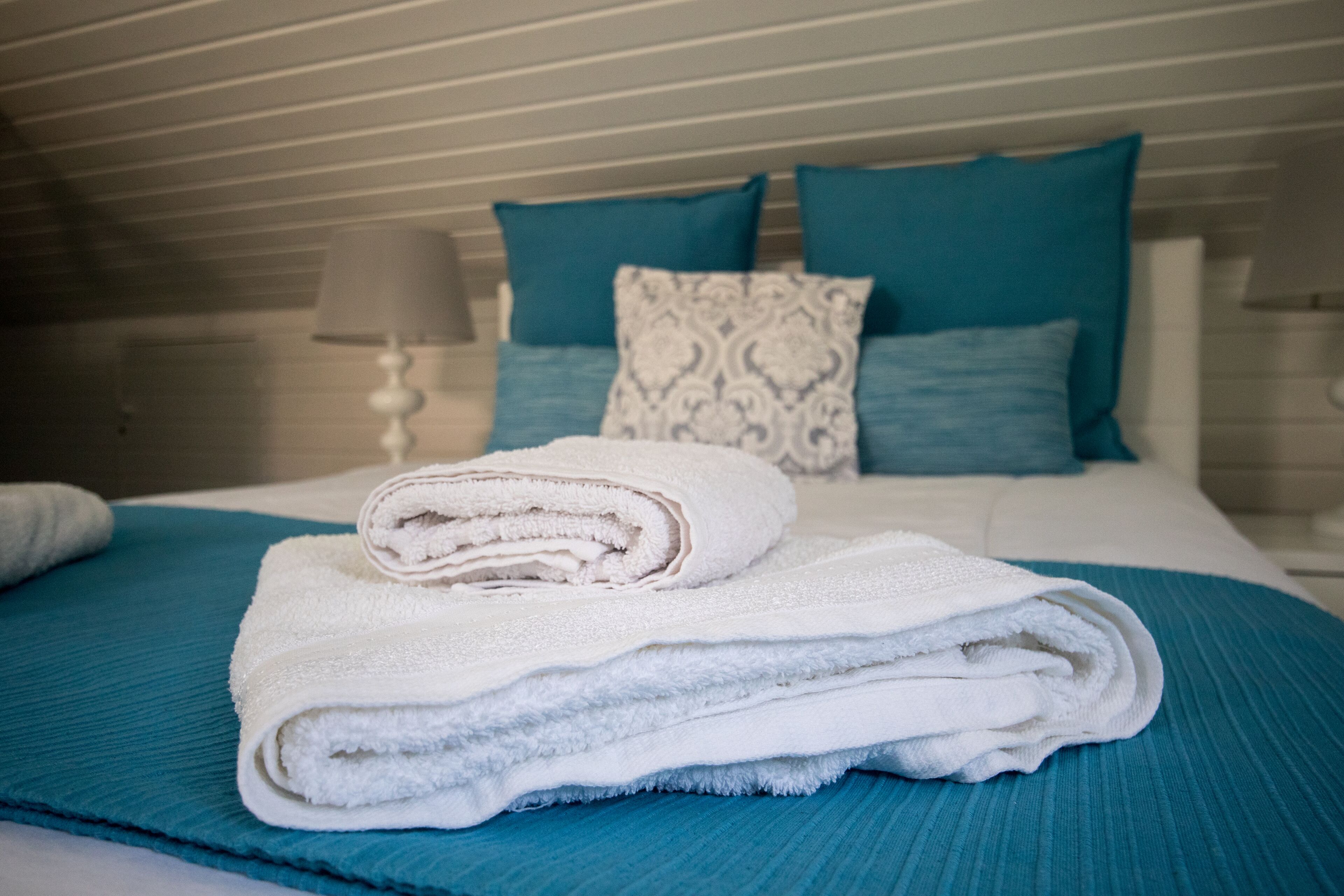 Cama bem arrumada com colcha verde-água, almofadas brancas e toalha branca dobrada.