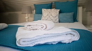 A neatly made bed with a teal bedspread, white pillows, and a folded white towel. - Grannies House - Where Comfort and Relaxation Happens (Machico)