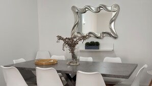 A dining area with a rectangular table, white chairs, a vase with dried flowers, a mirror on the wall, and a ceiling light fixture. - Grannies House - Where Comfort and Relaxation Happens (Machico)