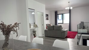 A modern living room with a grey sofa, white chairs, a dining table, and a red rug. - Grannies House - Where Comfort and Relaxation Happens (Machico)