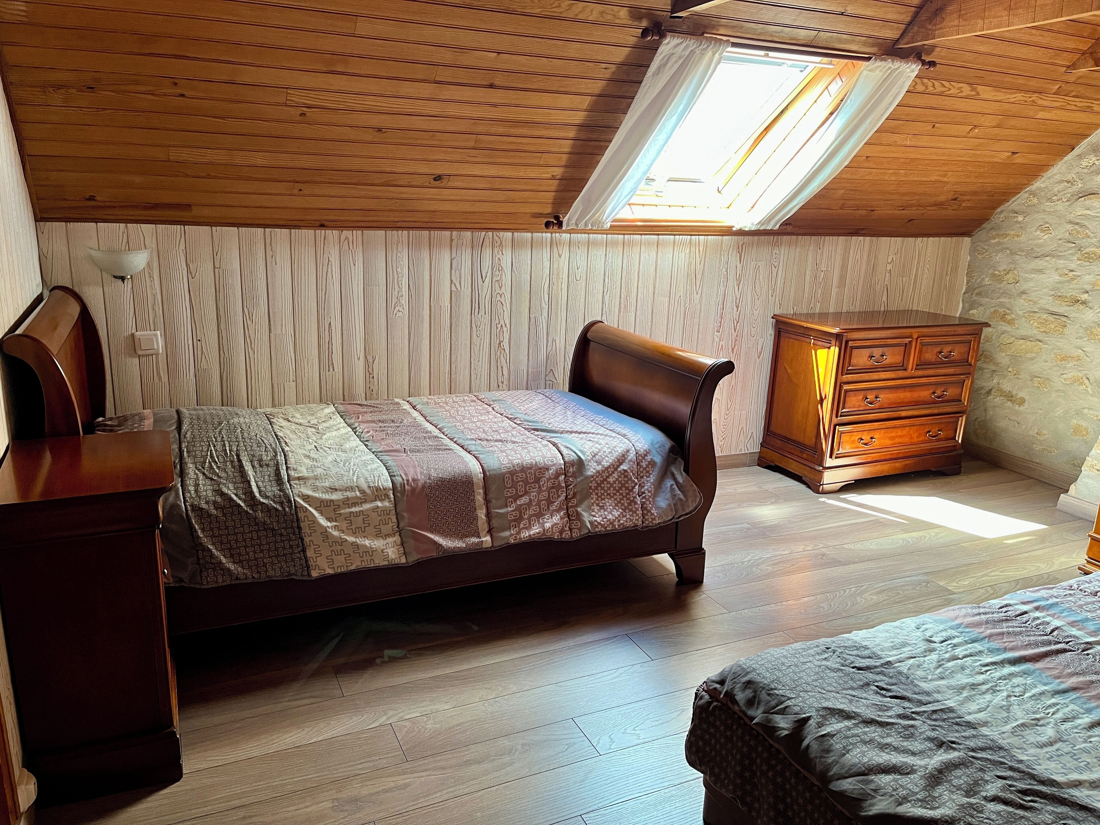 Una camera da letto con soffitto spiovente, un letto e un comò in legno e un piccolo tavolo.
