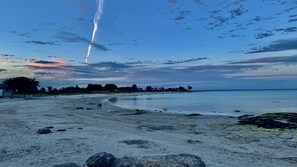 Een strand met een heldere lucht, kalme zee en een verre kustlijn met huizen.