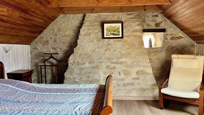 Une chambre mansardée chaleureuse avec un plafond en pente, des murs en pierre, un lit en bois, une chaise et un tableau encadré.