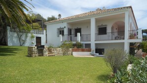 Una casa de dos pisos con una escalera de piedra que lleva a la entrada, rodeada de un césped cuidado y diversas plantas.