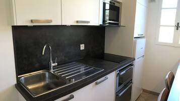 Een kleine keuken met een zwart aanrecht, een roestvrijstalen spoelbak, een inbouwoven en een kleine koelkast.