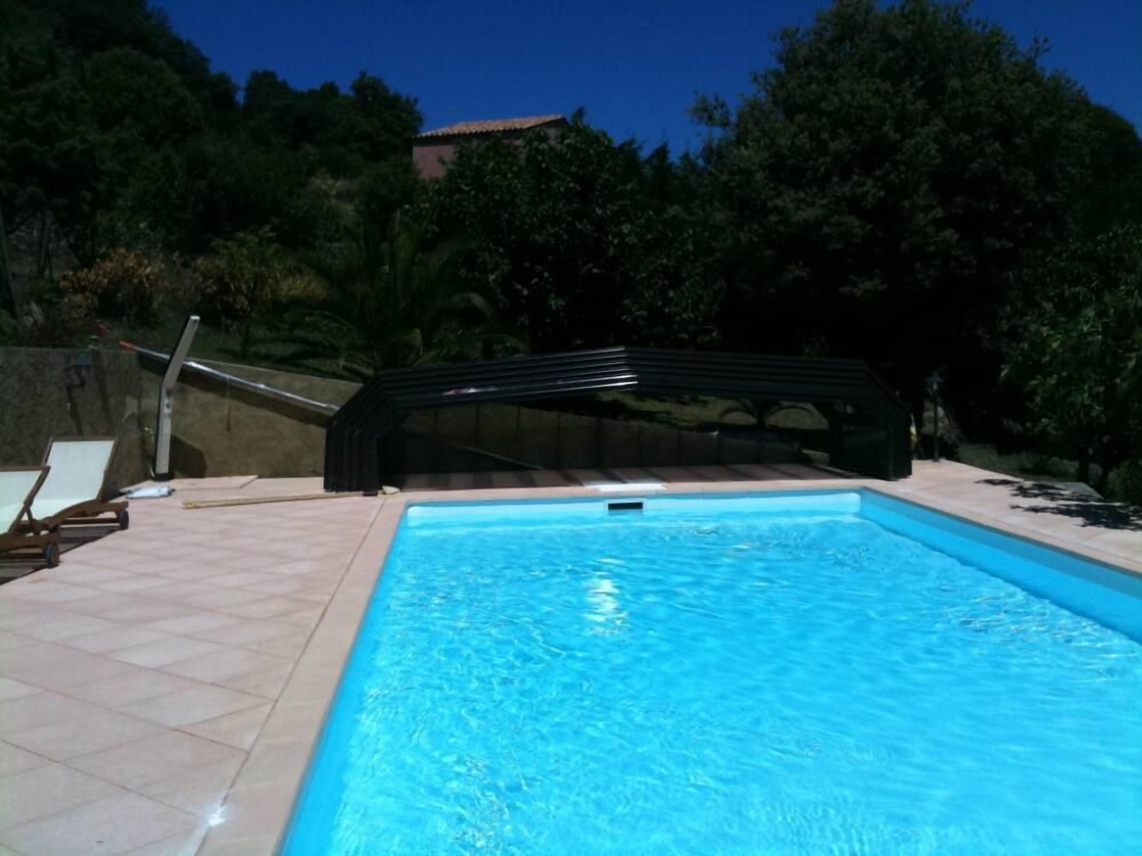 A swimming pool with a tiled deck, a covered area, and lounge chairs.